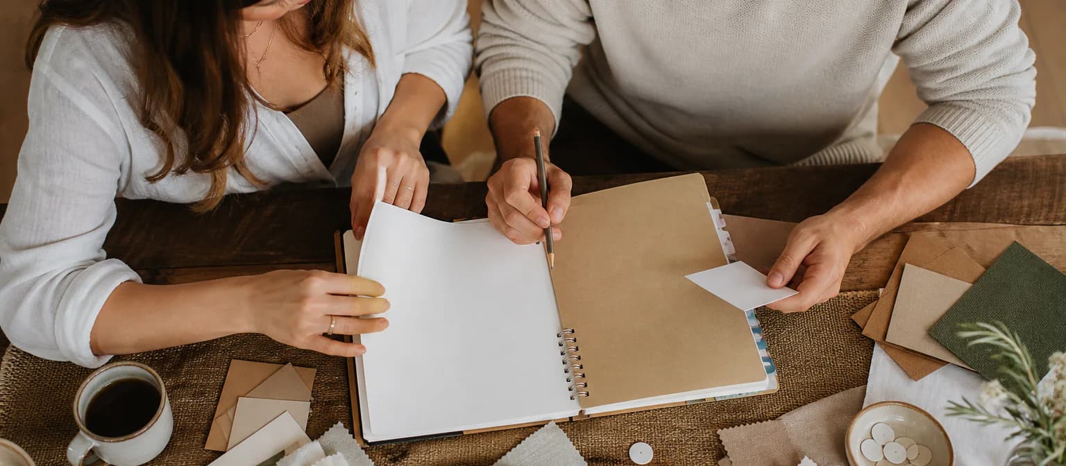 Two partners build a practical wedding planning notebook with blank dividers and material swatches.